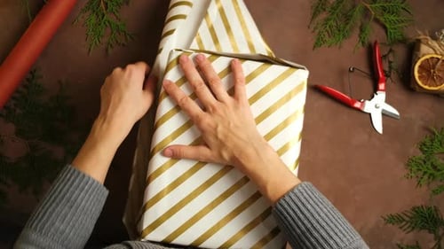 Hands Wrapping a Christmas Gift with Gold Stripes