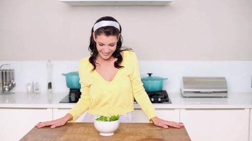 Smiling Woman Holding Bowl of Green Salad in Kitchen
