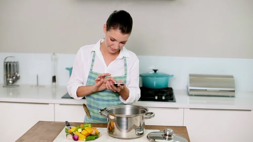 Woman Uses Smartphone While Preparing Vegetables in Kitchen