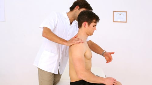 Chiropractor Adjusting Young Man's Back in Clinic