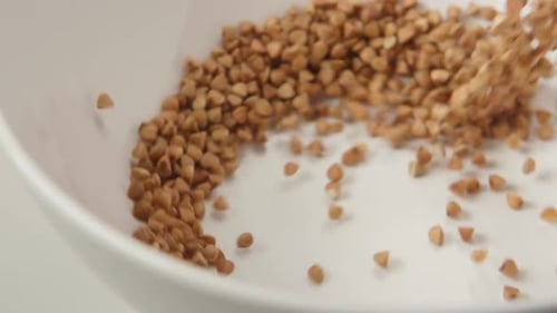 Buckwheat Grains Pouring into a White Ceramic Bowl