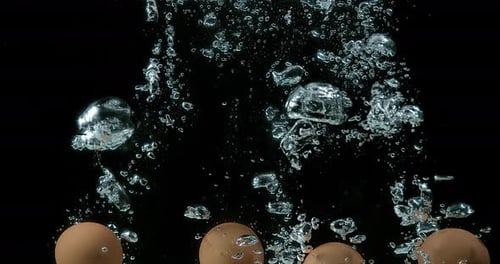 Hühnereier kommen vor schwarzem Hintergrund ins Wasser, Zeitlupe 4K