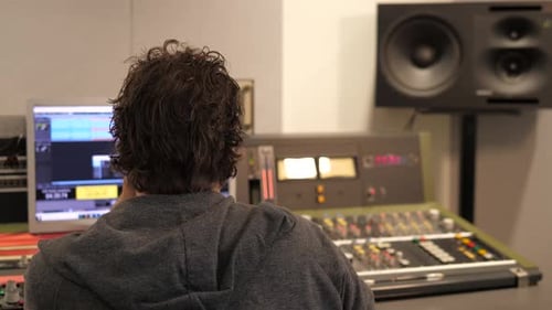 Sound engineer at work in music producing studio with mixer and computer