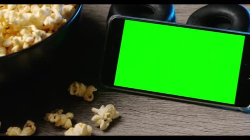 Popcorn in a big bowl and smart phone with green touch screen on the table.