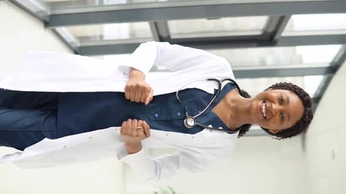 A Young African American Female Doctor or Nurse Stands in a Medical Suit at the Clinic and Looks at