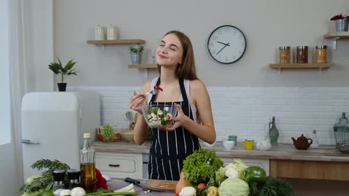 Woman Prepares and Tastes Salad in Bright Kitchen
