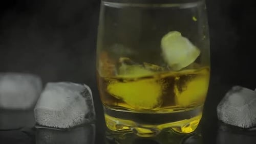Whiskey with Ice. Adding Ice Cubes on Black Background. Glass of Rum Alcohol