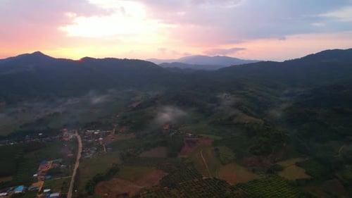 aerial view A drone fly over a rural area with mountains in the background at sunrise.