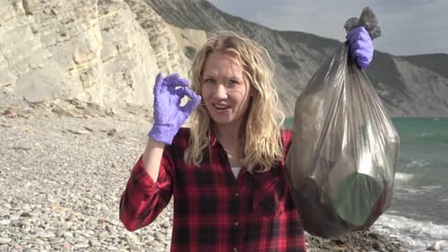 Retrato de una mujer voluntaria ambiental con una bolsa de basura en la orilla del mar