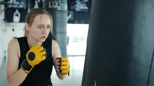 Motivated Kickboxer Wearing Gloves Training with Punching Bag Indoors in Gym