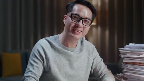 Close Up Of Asian Man Crossing Arms And Smiling To Camera While Working With Documents At Home