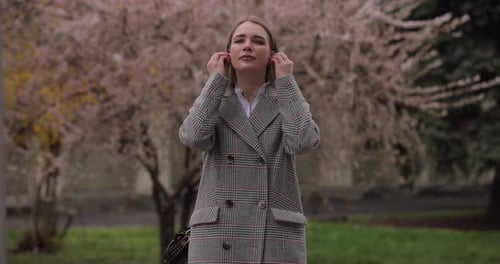 Woman Puts Earbuds in at Park in Spring