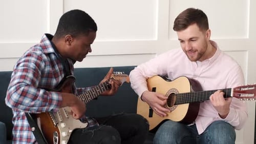 Two Men Play Guitars Together on a Couch