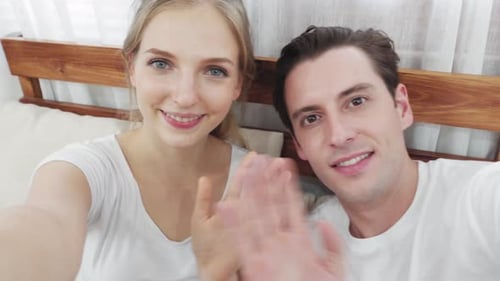 Young Couple Smiling and Waving in Bed