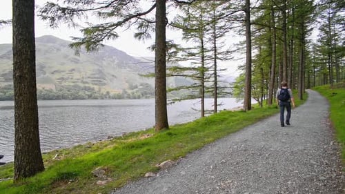A man walking on a road by the beautiful and peaceful lake in the England Lake District - wide shot