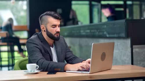 Programmeur indépendant masculin attrayant faisant des affaires en discutant en tapant à l'aide d'un ordinateur portable au Cozy Cafe