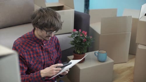 Young Adult Photographing Document Amongst Moving Boxes