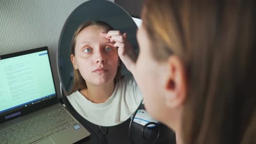 Junge Frau schaut sich im Spiegel an, untersucht ihre Gesichtshaut und regt sich auf