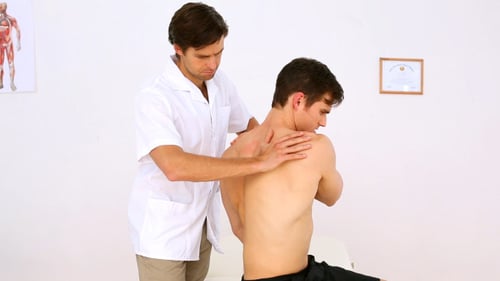 Chiropractor examining young adult male's shoulder