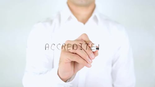 Man Writing Accredited on a Clear Surface