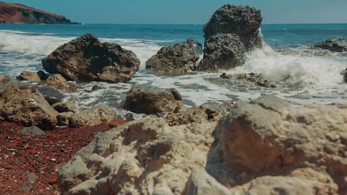 Slider-Aufnahme eines Vulkanstrandes am Mittelmeer mit rotem Sand und Brandung, die auf die Felsen trifft