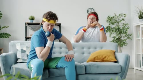 Man Lifting Dumbbell as Another Eats Hamburger
