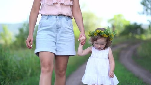Glückliche Mutter und Tochter mit dem Blumenkranz auf dem Land spazieren