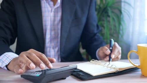 Close Up of Man Hand Using Calculator and Writing on Notepad