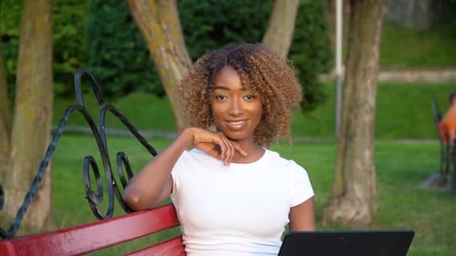 Woman Using Laptop on Bench in Sunny Park