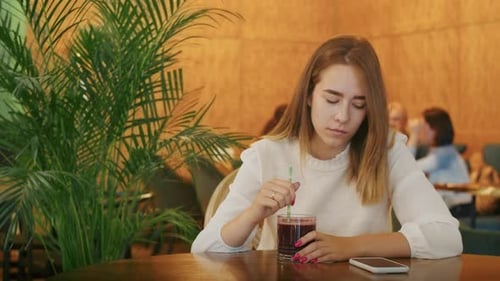 Joyful Girl Drinking Tea in a Cafe and Talking on the Phone or Video Call