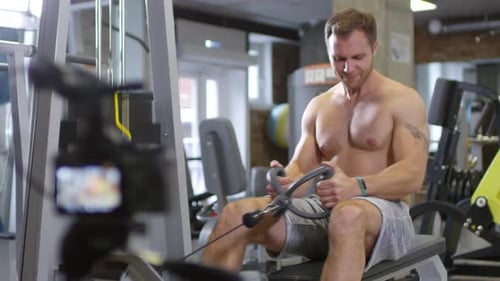 Shirtless Athlete Talking on Camera and Using Cable Row Machine