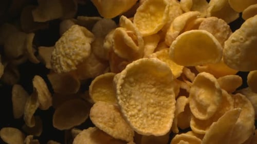 Golden Corn Flakes Floating Against Dark Background