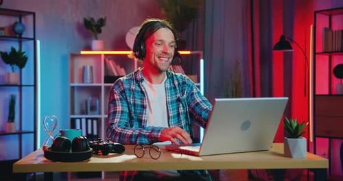 Young Man Excitedly Gaming on Laptop at Desk