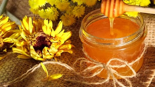 Honey Dripping Into a Jar with Yellow Flowers