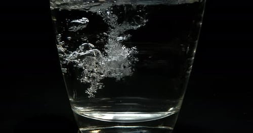 Wasser wird vor schwarzem Hintergrund in Glas gegossen, Zeitlupe 4K