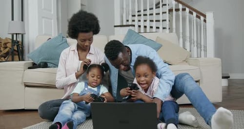 Pareja afroamericana con sus dos hijas pequeñas sentadas en el suelo y jugando a un videojuego