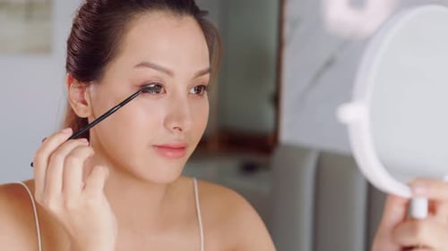 Woman Applies Mascara Looking in Mirror at Home