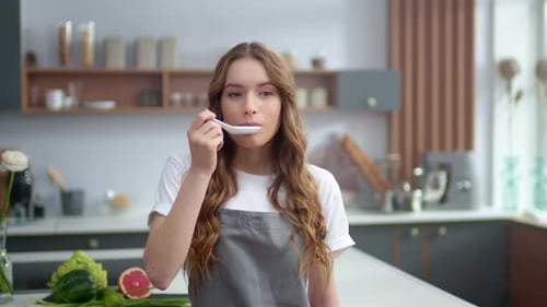 Woman Tasting Food in Kitchen with Spoon