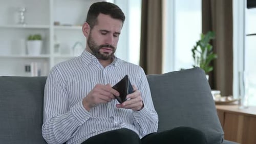 Besorgter junger Geschäftsmann checkt zu Hause leere Brieftasche