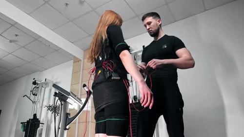 Ein Mann befestigt Kabel am EMS-Fitnessanzug der Frau