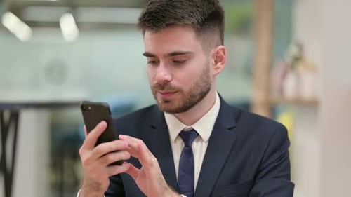 Man Celebrates Success on Smartphone Indoors