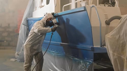 Worker Paints Vehicle with Spray Gun in Factory
