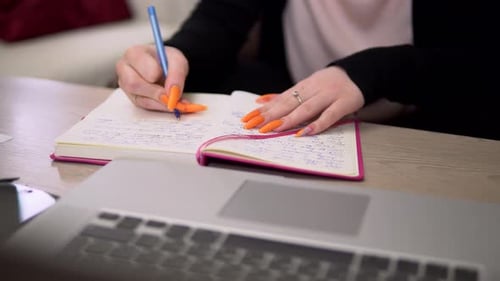 Woman Writing in Notebook at Desk with Laptop