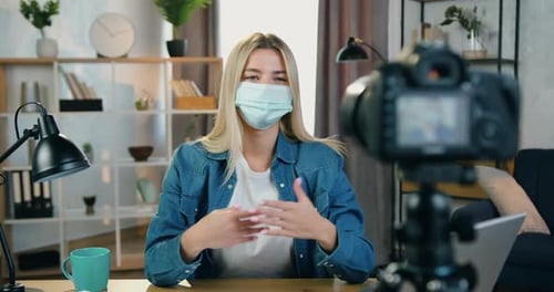 Mujer con máscara facial grabando Vídeo en cámara en un estudio casero para su audiencia de Internet