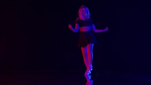 Young Woman with Long Blond Hairs Dances in Colorful Stage Lights in Studio