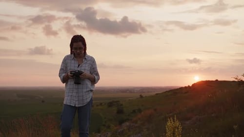 Woman Photographer Exploring Grassy Hills at Sunset