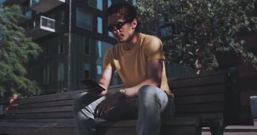 Man smiles while using phone on park bench