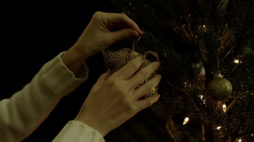 Hands Decorate Christmas Tree with Gold Ornaments