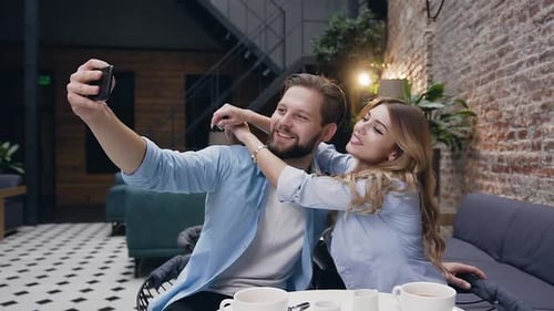 Blond Woman Hugging Her Joyful Bearded Boyfriend by Neck During Making Funny Selfie