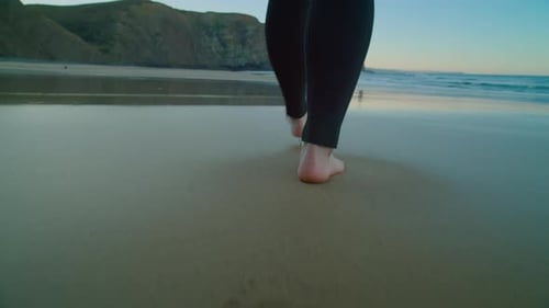 Kamera folgt Barfußsurfer im Neoprenanzug am Strand